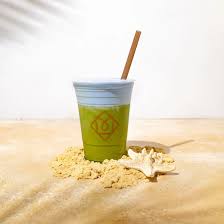 A 'Seafoam Mist' latte in a clear double-walled glass. The drink has distinct layers of deep seafoam green matcha and creamy white milk, topped with a light, airy foam and a sprinkle of gold dust.